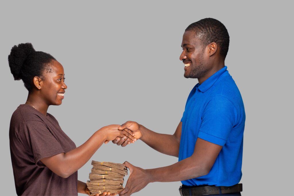 Tanzanian loan officer handing a stack of money to a smiling woman with one hand, while shaking her hand with the other, symbolizing successful loan disbursement and trust.